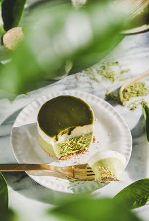 Green matcha cheesecake on plate over green leaves and grey marble table background, top view, selective focus. Healthy, vegan, vegetarian, low calorie food conceptの写真素材