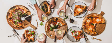 Pizza party for friends or family. Flat-lay of various pizzas, drinks and people celebrating over plain white table background, top view. Fast food, comfort food, Italian cuisine conceptの写真素材