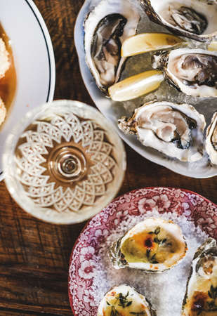 Flat-lay of oven baked oysters with parmesan cheese and herbs and fresh oysters with lemon in colorful plates in fish restaurant, top view. Seafood cuisine, fine dining conceptの写真素材