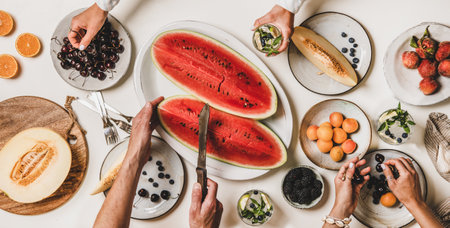 Summer tropical fruit party table. Flat-lay of peoples hands taking food from table with various fruits, berries, watermelon and lemonade, top view. Clean eating, vegan, fruitarian food conceptの写真素材