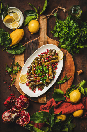 Turkish traditional starter meze. Flat-lay of Turkish Sarma wine leaves filled with rice and spices with pomegranate, olive oil, greens over rusty table background, top view. Turkish regional cuisineの写真素材