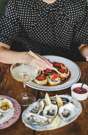 Girl eating baked susi maki with chopsticks over fresh oysters on table at Japanese restaurant, selective focus. Japanese cuisine, fast food, seafood, fine dining conceptの写真素材