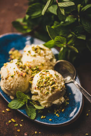 Turkish traditional dessert semolina helva. Scoops of sweet semolina helva with pistachio nuts and fresh mint leaves on blue plate over rusty table background, selective focus. Turkish cuisineの写真素材