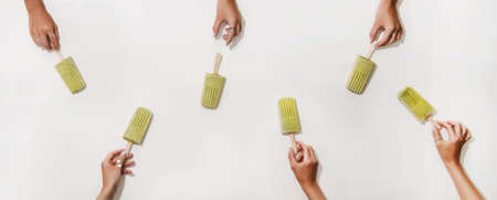 Green matcha coconut vegan ice cream . Flat-lay of womens hands taking matcha ice cream from plain white table, top view. Summer healthy dessert, clean eating, dairy free food conceptの写真素材