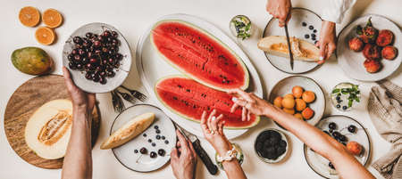 Summer tropical fruit party table. Flat-lay of peoples hands with various fruits, berries, watermelon and lemonade over white background, top view. Clean eating, vegan, fruiterian food conceptの写真素材