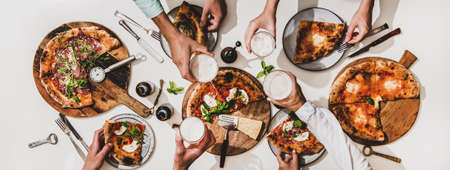 Pizza party for friends or family. Flat-lay of various pizzas, drinks and people celebrating with beer over plain white table background, top view. Fast food, comfort food, Italian cuisine conceptの写真素材