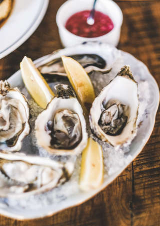Fresh Irish oysters with lemon and red onion sauce over ice in plate on restaurant table, selective focus. Seafood, French cuisine, fine dining conceptの写真素材