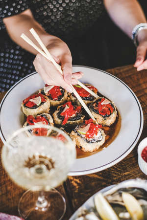 Girl eating baked susi maki with chopsticks over fresh oysters and champagne on table at Japanese restaurant, top view, selective focus. Japanese cuisine, fast food, seafood, fine dining conceptの写真素材