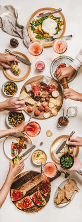 Family wine and snack party. Flay-lay of peoples hands eating and drinking rose wine over table with cheese, fruit, smoked meat, tomato brushettas, buratta salad, top view. Wine tasting conceptの写真素材