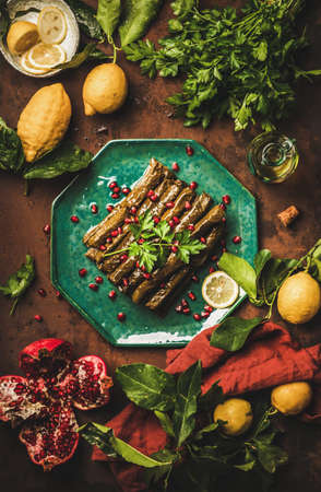 Turkish traditional starter meze. Flat-lay of Sarma wine leaves filled with rice, spices with pomegranate, olive oil, greens, lemon over rusty table background, top view. Turkish regional cuisine foodの写真素材