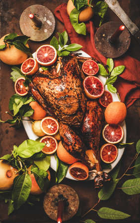 Christmas or Thanksgiving Day festive table setting. Flat-lay of whole roasted turkey with citrus fruit with candles over rustic rusty table background, top view. Holiday gathering foodの写真素材