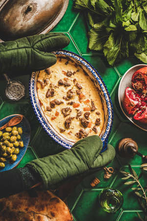 Turkish style family dinner concept. Flat-lay of cooks hands in gloves putting stewed lamb in yogurt sauce on table with flatbread, fruits and olives, top view. Ramazan iftar, gathering supperの写真素材
