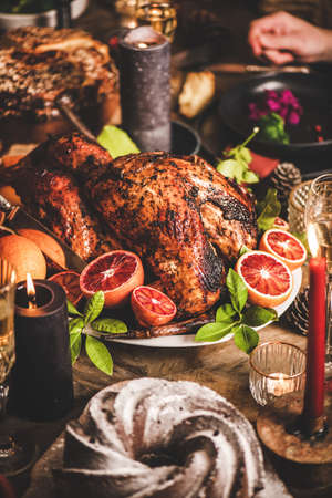 Family or friends celebrating Christmas or New Year. Holiday rustic wooden table with roasted turkey, chocolate cake, champagne and candles, red brick wall at backgroundの写真素材