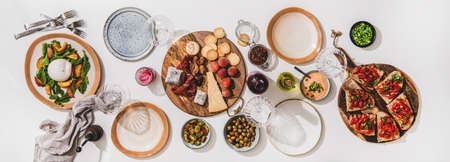 Family wine and snack party. Flay-lay of wineglases, boards with cheese, fruit, smoked meat, tomato brushettas, buratta salad over white table background, top view. Wine tasting, celebration conceptの写真素材