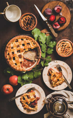 Autumn tea time setting. Flat-lay of apple and plum pie on rack with tea in pot over dark rusty table background, top view. Fall sweet comfort food conceptの写真素材