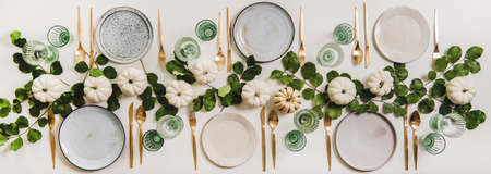 Fall table setting for celebration Thanksgiving or Friendsgiving day, family party or gathering. Flat-lay of plates, cutlery, glassware, pumpkins and leaves over plain white table background, top viewの写真素材