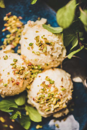 Turkish traditional dessert semolina helva. Close-up of scoops of sweet semolina helva with pistachio nuts and fresh mint leaves over rusty table background, selective focus. Turkish cuisineの写真素材