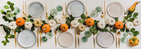 Fall table setting for celebration Thanksgiving or Friendsgiving day, family party or gathering. Flat-lay of plates, cutlery, glassware, colorful pumpkins and leaves over white background, top viewの写真素材
