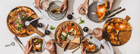 Pizza party for friends. Flat-lay of various pizzas, lager beer and peoples hands with pizza slices and glasses over white table background, top view. Fast food, comfort food, Italian cuisine conceptの写真素材