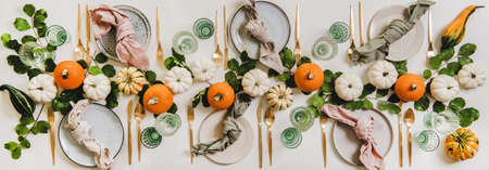Autumn Thanksgiving festive table decoration setting for Fall gathering or family party. Flat-lay of plates, cutlery, floral decoration with pumpkins and leaves over white table background, top viewの写真素材