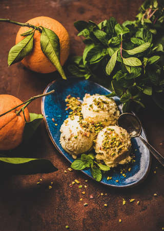 Turkish traditional dessert semolina helva. Scoops of sweet semolina helva with pistachio nuts, fresh mint and tangerines over rusty table background, top view. Turkish cuisineの写真素材