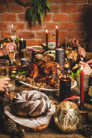 Christmas or New Year holiday party table setting. Hands of people sitting at festive table with roasted Turkey with Rice and chestnuts, bundt cake, candles and Champagne, brick wall backgroundの写真素材
