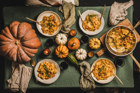 Flat-lay of Autumn dinner for gathering or Thanksgiving Day celebration party. Butternut squash pasta with sausage and sage in plates and red wine in glasses over linen tablecloth, top viewの写真素材