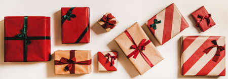 Flat-lay of festive craft gift boxes in wrapping paper decorated with ribbons and green and red bows over plain white background, top view. Christmas boxing day conceptの写真素材
