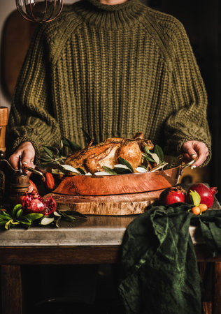 Female in knitted sweater holding whole roasted chicken for winter holiday festive dinner in copper roasting tin with spices, herbs and fresh fruit. Christmas or Thanksgiving Day cooking conceptの写真素材