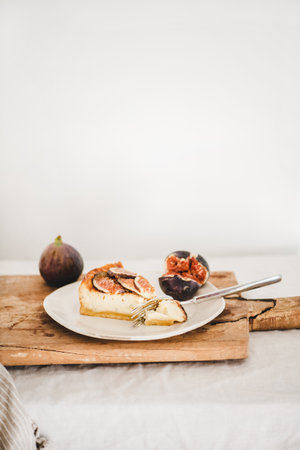 Slice of homemade fig cheesecake with fresh figs and fork on white plate over rustic wooden board, white wall at background, copy space. Healthy dessert, artisan sweet food conceptの写真素材