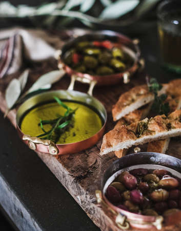 Pickled Greek olives, olive oil in copper jars and herbed focaccia slices on rustic wooden board, selective focus, close-up. Traditional Mediterranean meze appetizers platterの写真素材