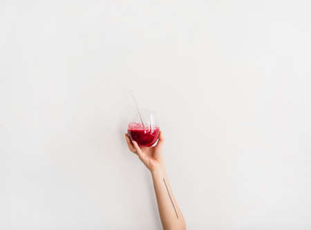 Human hand holding glass with purple beet pomegranate fresh homemade smoothie with glass straw,...