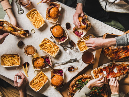 Lockdown family fast food dinner from delivery service. Flat-lay of friends group eating burgers, fries, sandwiches, pizza, drinking beer at home party over table background, top viewの写真素材