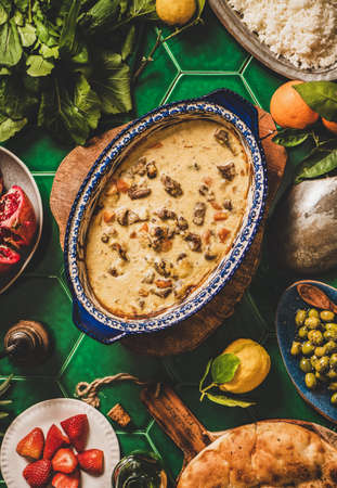Turkish style family dinner. Flat-lay of lamb in yogurt sauce and ingredients for pilav and fresh salad over green tile table with flatbread, top view. Ramazan iftar, gathering, celebration supperの写真素材