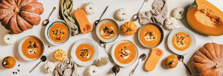 Flat-lay of seasonal fall pumpkin cream soup served in plates with sour cream and pumpkin seeds over...