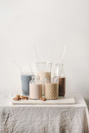 Dairy-free milk assortment with different flavours. Almond milk with blue matcha, berries, coffee, cinnamon, cocoa in bottles and glasses on counter, white background, copy space. Vegan, healthy foodの写真素材