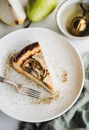 Piece of vegan dairy-free sugar-free homemade pear cheesecake in rustic plate and fresh pears over white marble table background, top view. Modern vegetarian healthy dessert conceptの写真素材