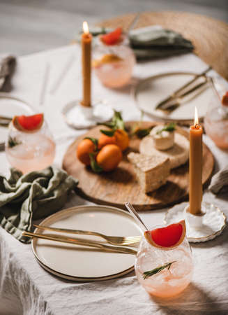 Home cocktail party table setting. Grapefruit rosemary margaritas, cheese fruit board, candle, dinnerware, cutlery on table. Romantic table setting for family celebration, stay at home during lockdownの写真素材