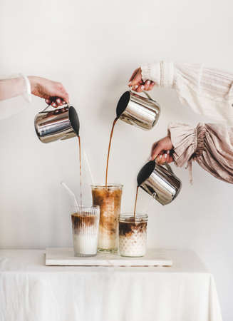 Female hands in elegant dress sleeves pouring fresh coffee to glasses with milkの写真素材
