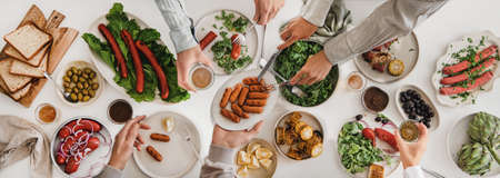 Flat-lay of hands eating pork sausages and drinking beer togetherの写真素材