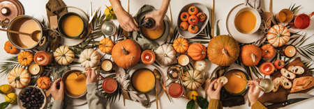 Hands of people eating pumpkin soup over decorated tableの写真素材