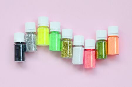 Colorful glitters lies on pastel pink background. Many round jars with multi-colored bright sparkles for nail polish. Sparkling sequinsの写真素材