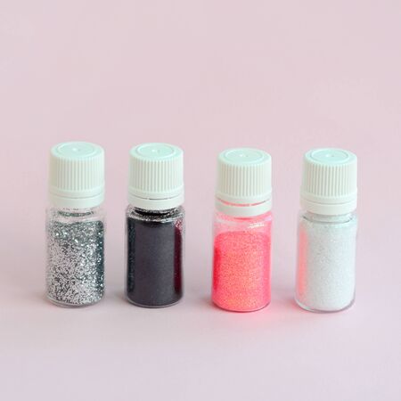 Colorful glitters lies on pastel pink background. Many round jars with multi-colored bright sparkles for nail polish. Sparkling sequinsの写真素材