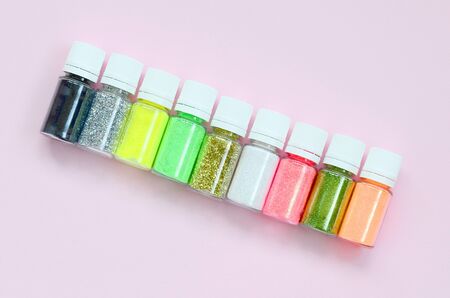 Colorful glitters lies on pastel pink background. Many round jars with multi-colored bright sparkles...