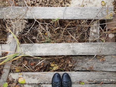 legs in jeans and boots stand on a wooden board of a broken old wooden bridge in autumnの写真素材