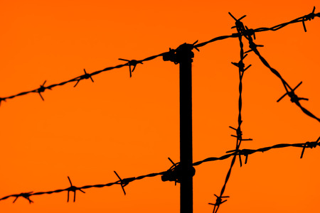 silhouette of a fence of barbed wire on an orange sky backgroundの写真素材