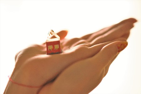 small toy rural house on female hands with a red thread on the wrist