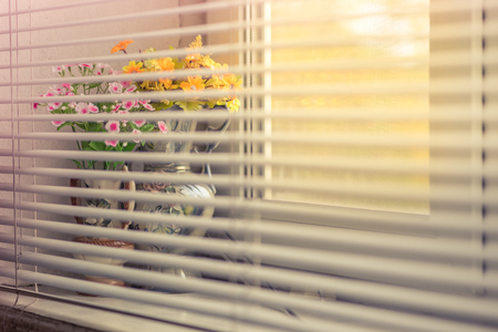 Bouquet of flowers in a vase on the windowsill behind covered blinds.の写真素材
