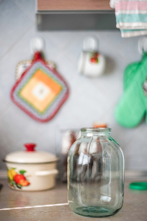 Empty three-liter jar is on the tabletop against the background of the pot and oven mitts, selective focusの写真素材