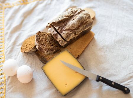 Slised black bread on a cutting board, a big slice of cheese and eggs lie on a table